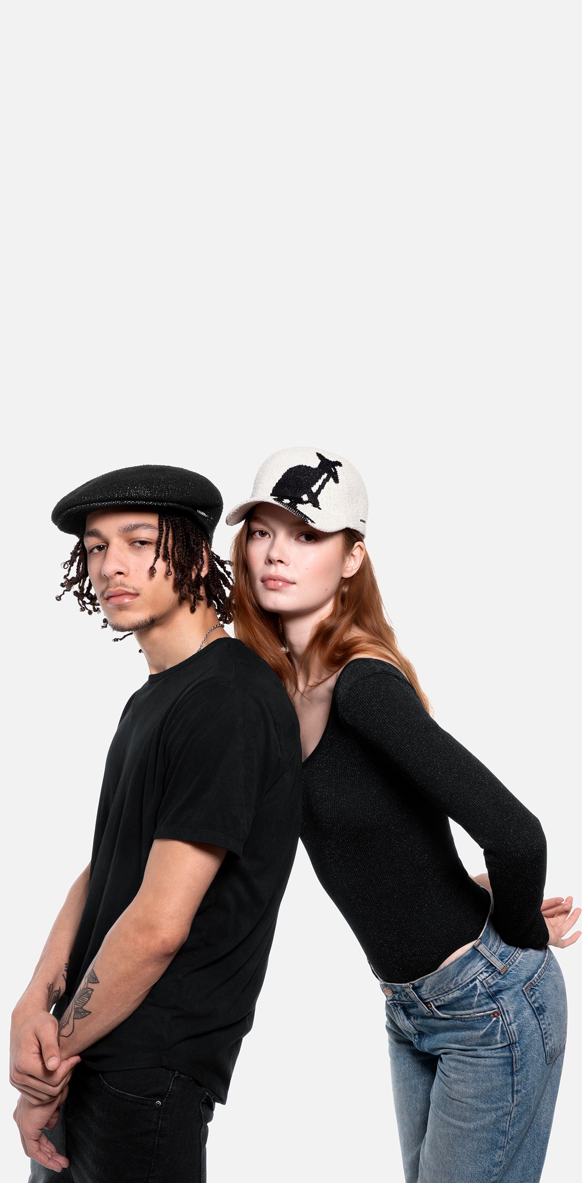 Two people wearing black tops and jeans against a white background