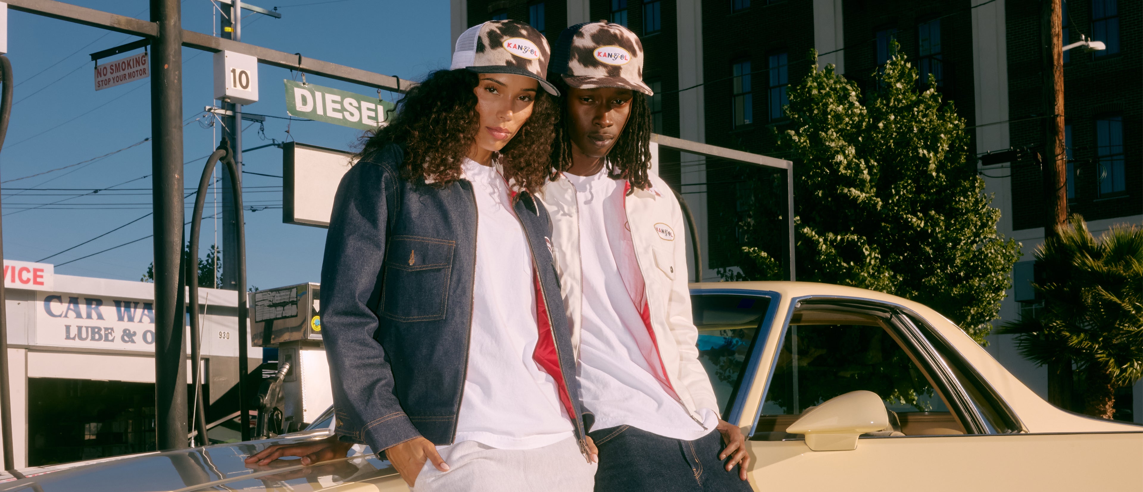 Two people wearing Kangol trucker hats standing next to a car in an urban setting with a visible 'DIESEL' sign.