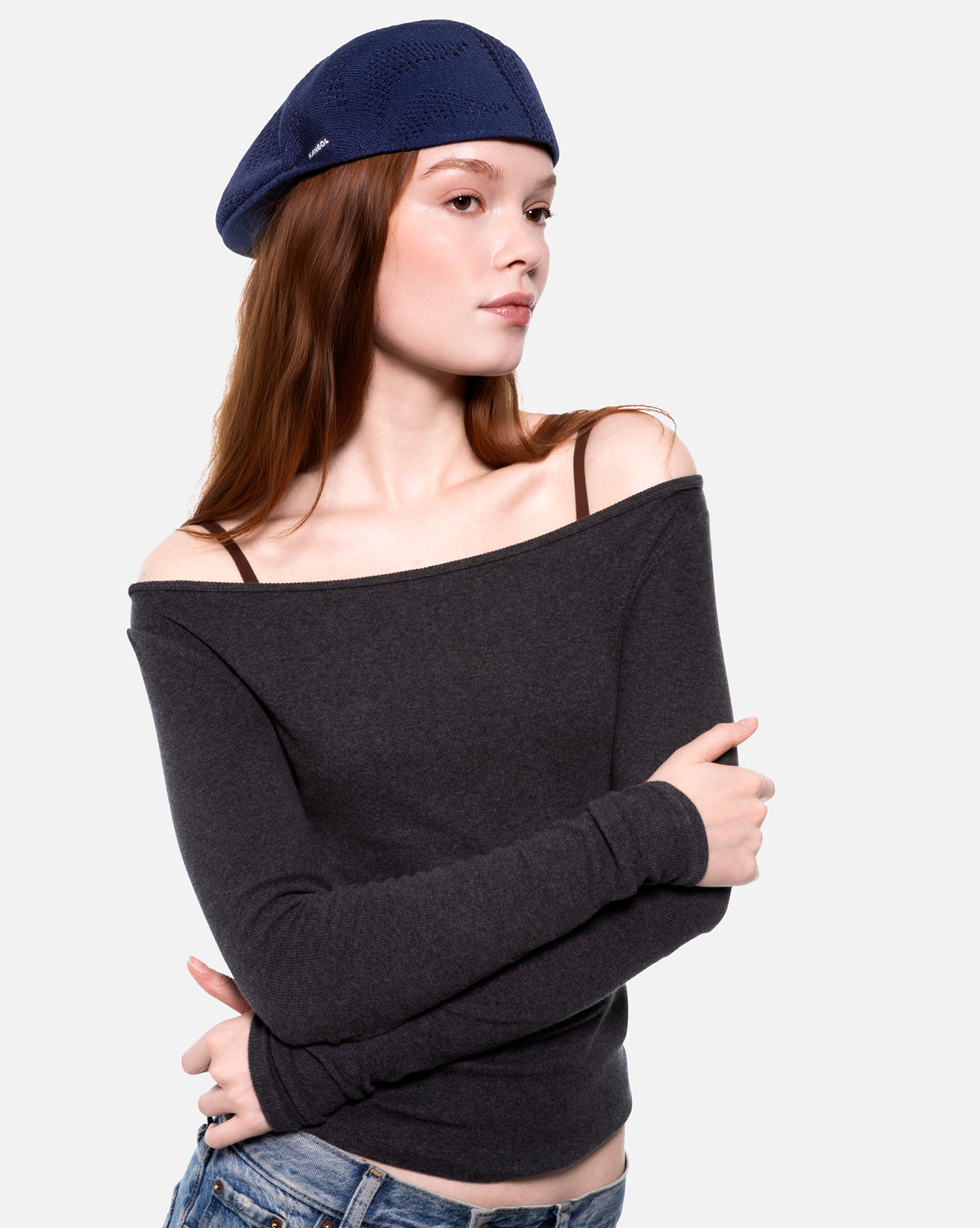 Woman wearing a navy flat cap backwards and off-shoulder black sweater on a white background