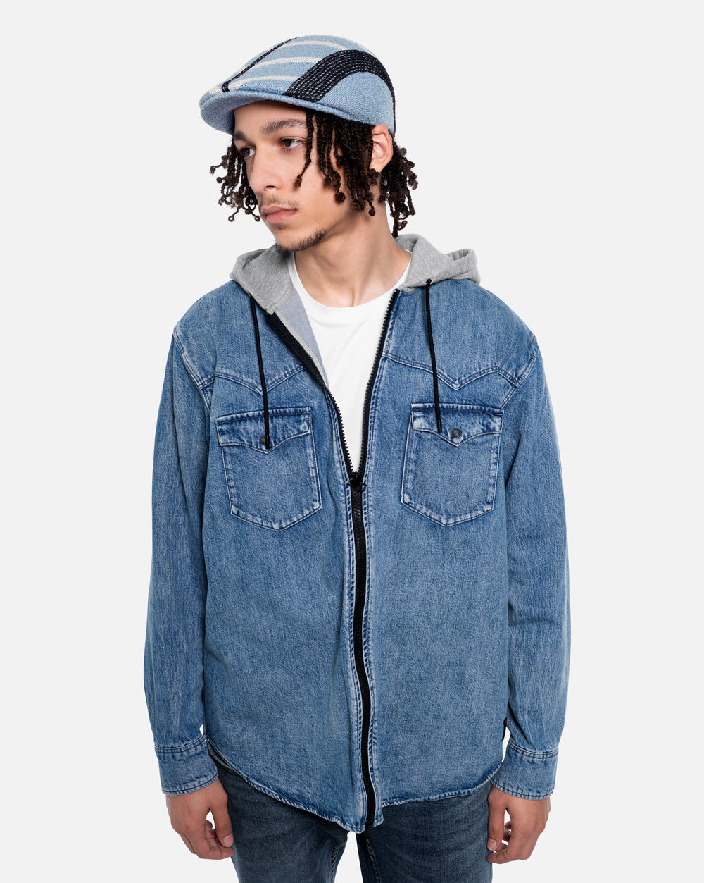 Person wearing a blue denim jacket with a hood and a light blue flat cap on a white background