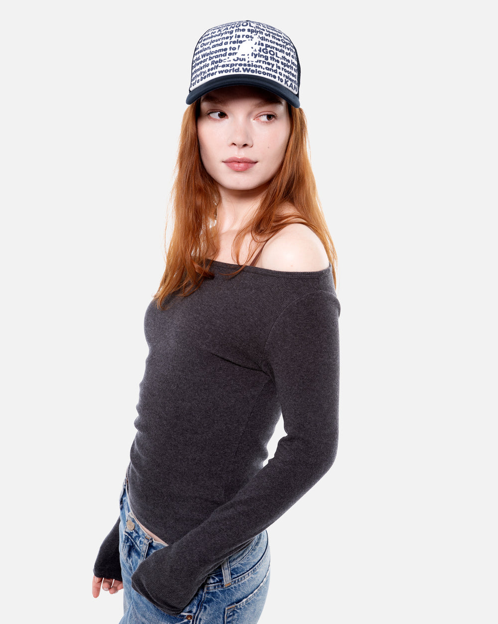 Woman wearing a dark gray off-shoulder sweater and printed trucker cap on a white background