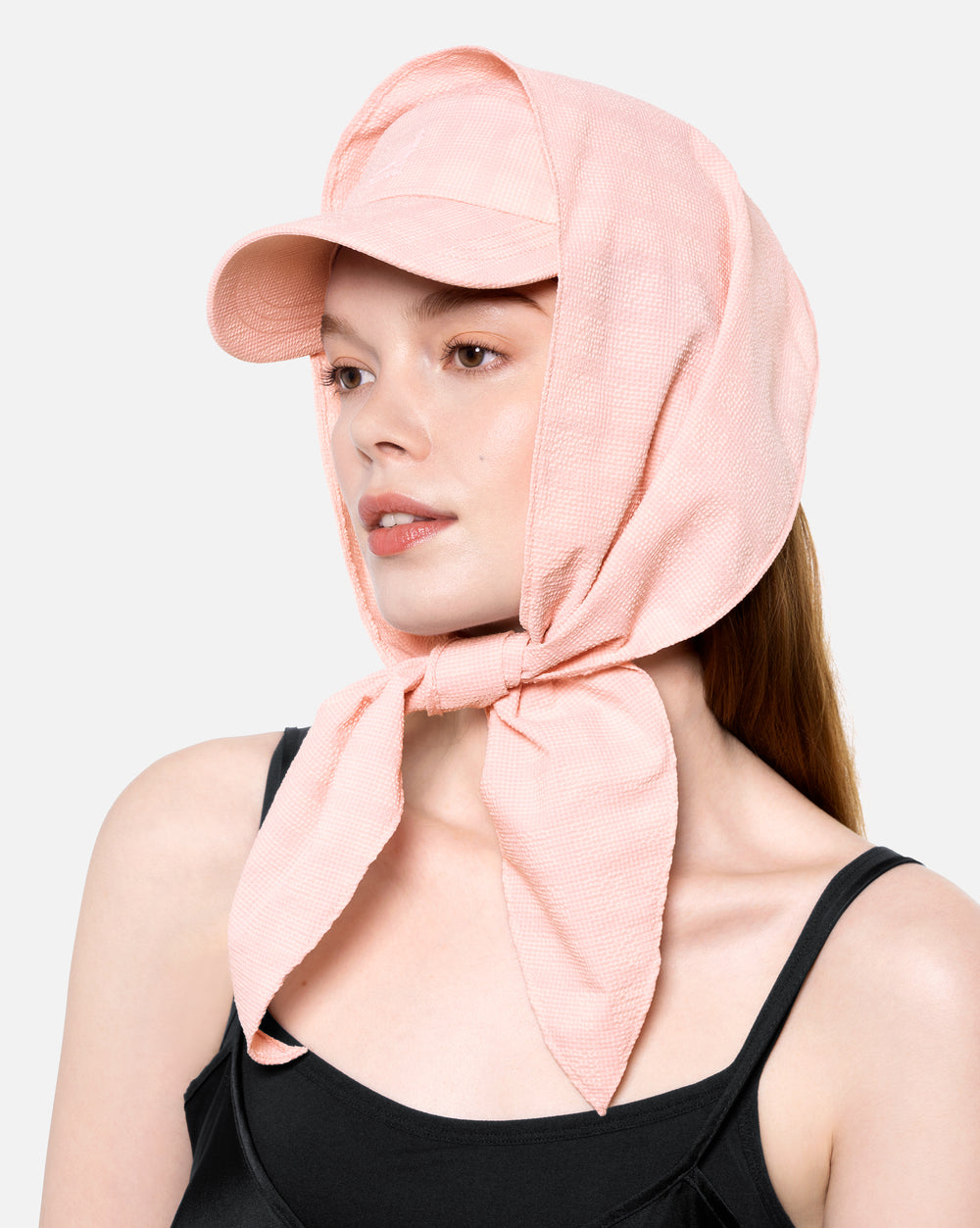 Woman wearing a pink headscarf and cap on a light gray background