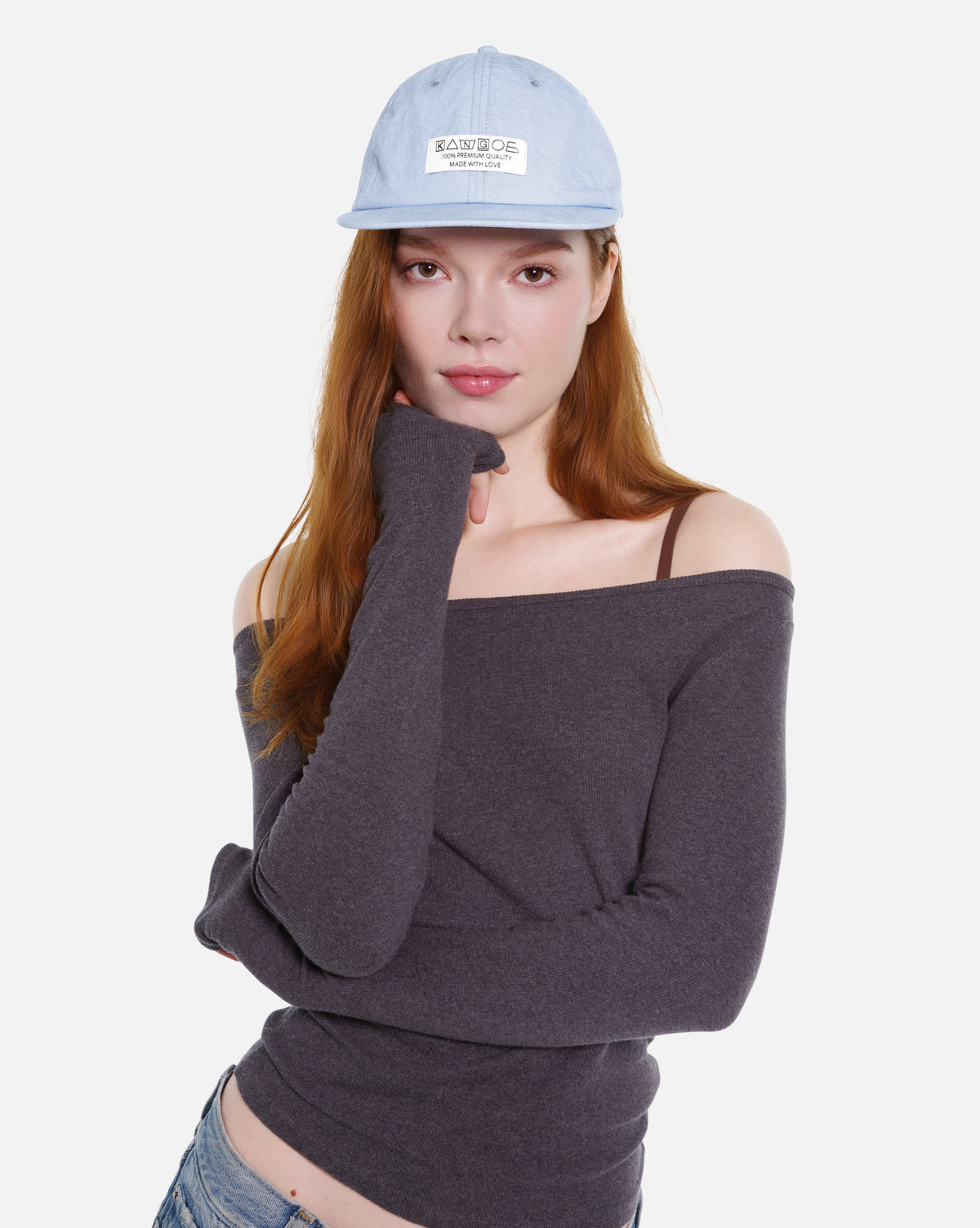 Woman wearing a gray off-shoulder sweater and light blue cap on a white background
