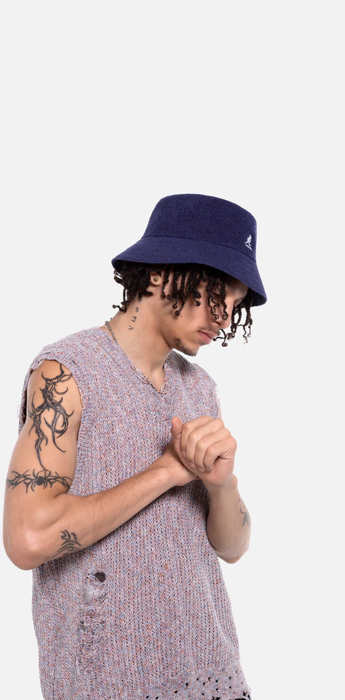Person wearing a navy bucket hat and sleeveless patterned shirt on a white background