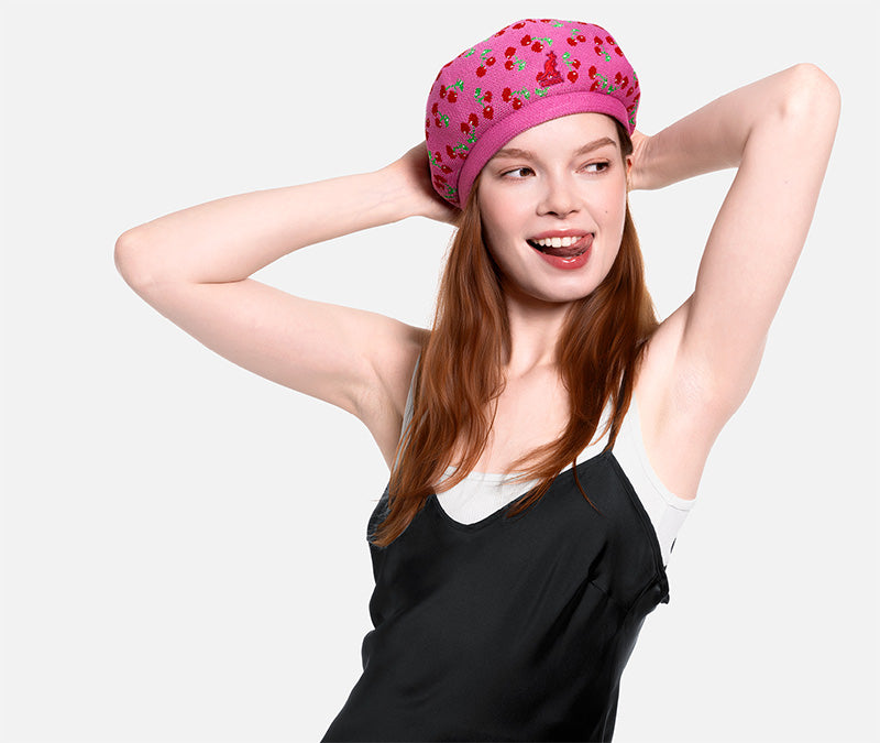 Woman wearing a pink cherry print beret on a plain background