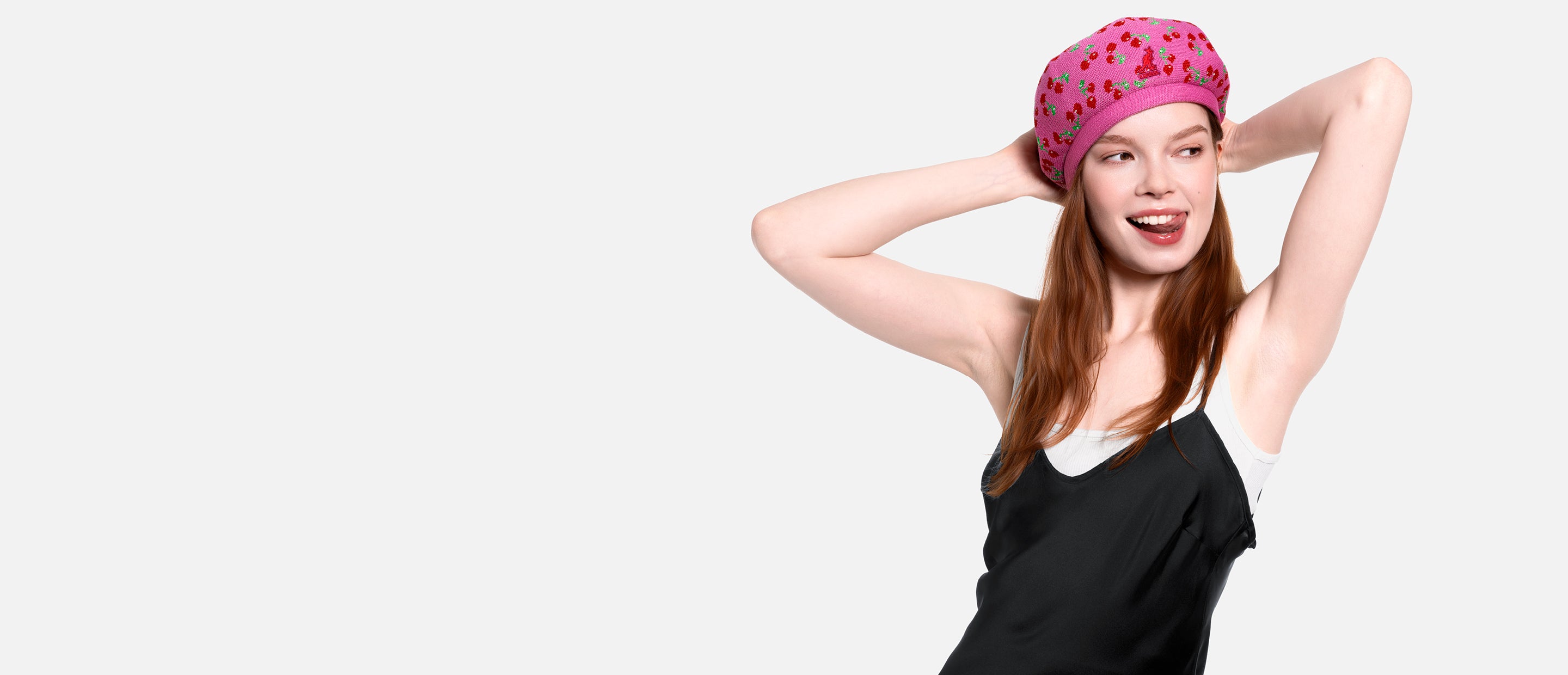 Woman wearing a pink cherry print beret and black top on a white background