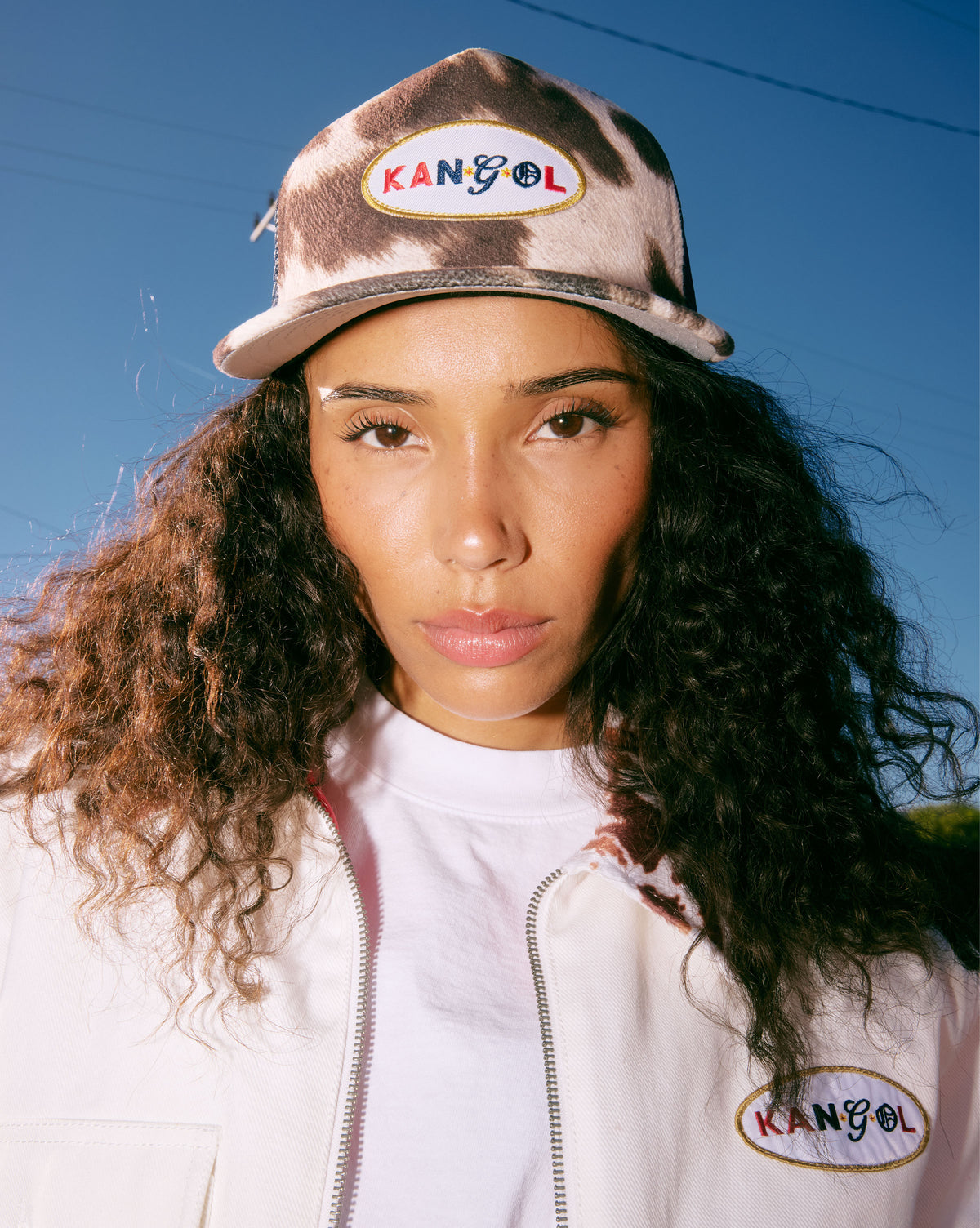 Person wearing a Kangol cap and jacket with a clear blue sky background
